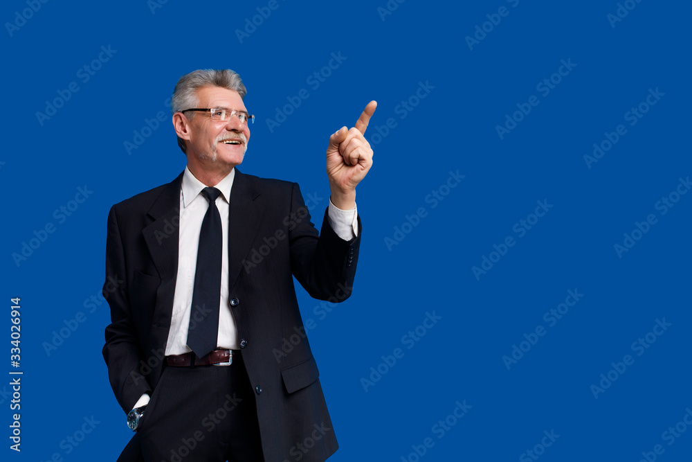 Happy senior business man pointing up at copy space while staying on blue background Happy senior business man pointing up at copy space while staying on blue background