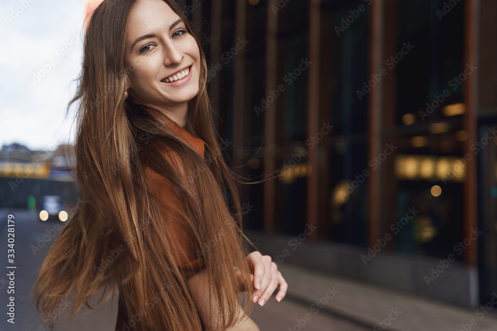 Fototapeta premium Women and business concept. Happy romantic young caucasian woman in brown fake-leather dress, turn behind to smile at camera, wind blowing at hair, lady feeling carefree and joyful