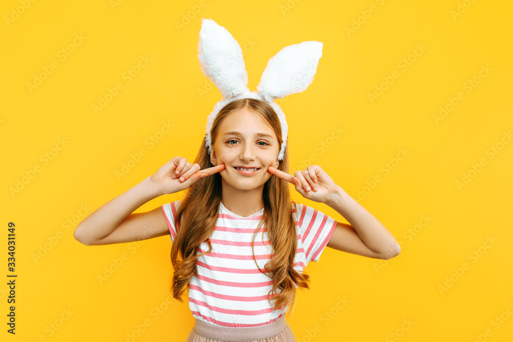 Happy little beautiful girl on her head with rabbit ears, posing on a yellow background