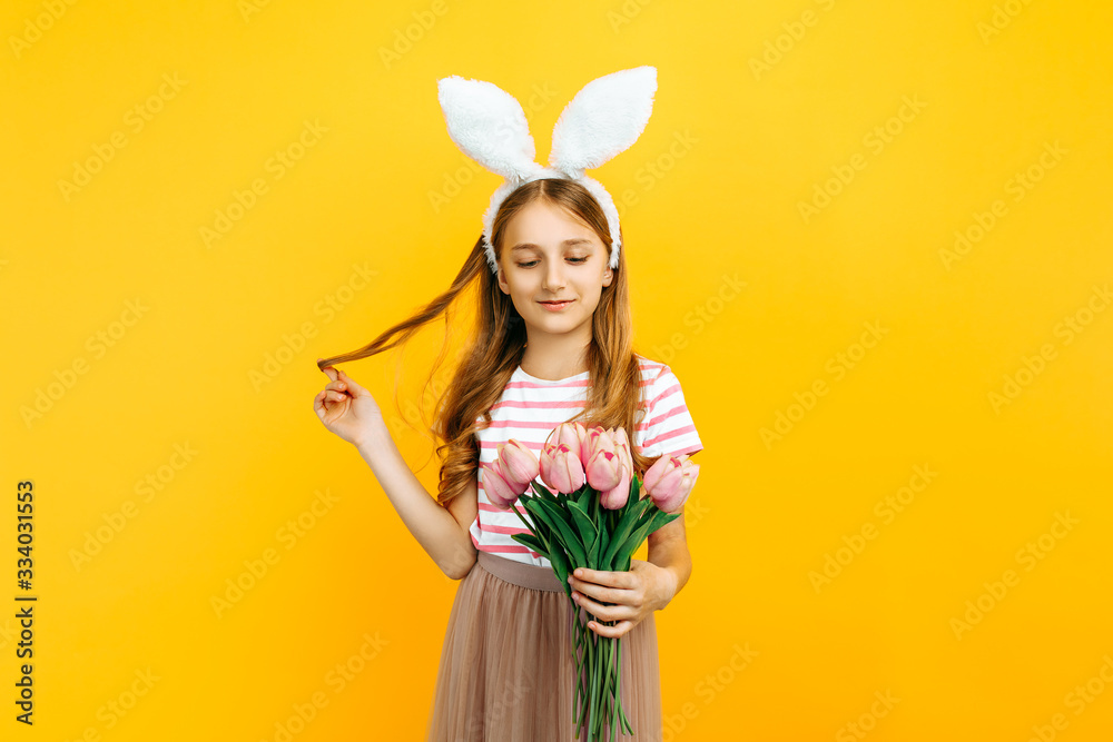 Happy beautiful girl on her head with rabbit ears, with a bouquet of tulips on a yellow background