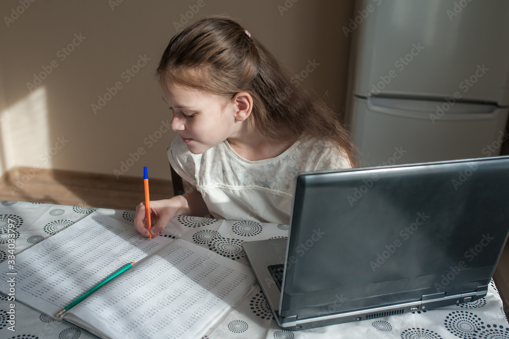 A school-age girl sits at home at a table and studies using a laptop. Distance Education, Quarantine A school-age girl sits at home at a table and studies using a laptop. Distance Education, Quarantine