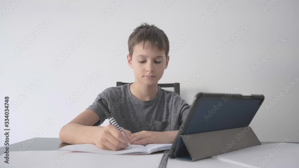 Online learning, distance lesson, education at home, technology for kids. Boy with textbooks doing school homework and using digital tablet computer at home Online learning, distance lesson, education at home, technology for kids. Boy with textbooks doing school homework and using digital tablet computer at home