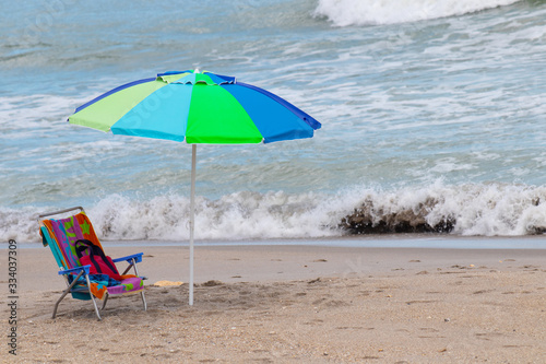 A blue and green umbrella all alone on a beach with ocean waves coming in