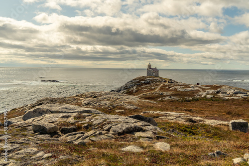 Historic lighthouse, distance view low, stone building, slate roof and sash window, a walkway around the light room gives the impression of a citadel, sits on a rocky shore of the Atlantic ocean,