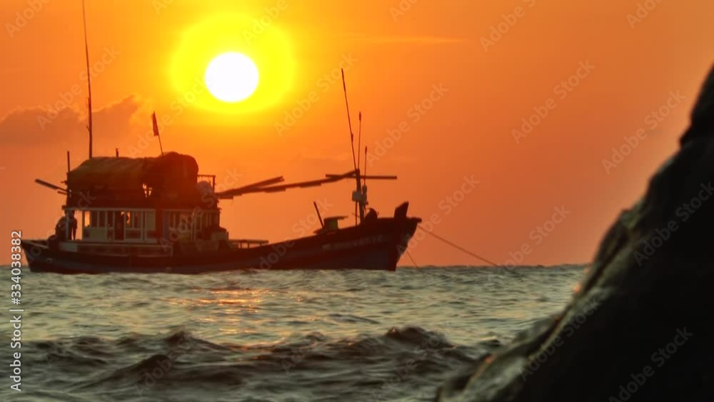 Silhouette of the anchored fishing boat in the rays of the setting sun swinging in the waves and a rocky birch in the foreground Silhouette of the anchored fishing boat in the rays of the setting sun swinging in the waves and a rocky birch in the foreground
