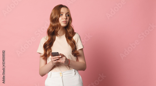 stylish young adult girl holding smart phone isolated on pink background
