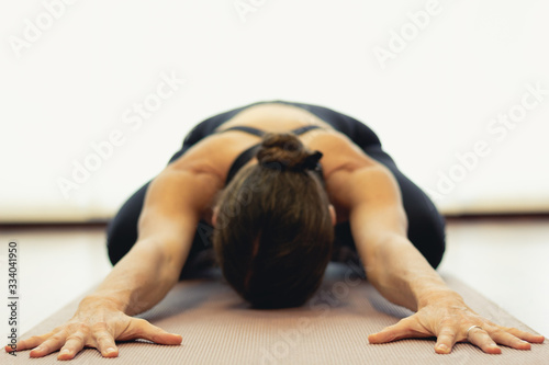 Yogi woman practices child pose in bright studio. Focus on hands of lady in balasana on purple mat. Healthy lifestyle, resting exercise, workout, sportswear, yin yoga concepts. Vintage effect applied