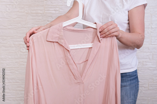 Caucasian woman choosing clothes, she is holding a hanger with beige blouse, shopping, fitting and buying clothes during sale and discount concept, cheap second hand clothes for online selling