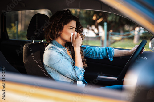 Photos Young woman sneezing while driving car