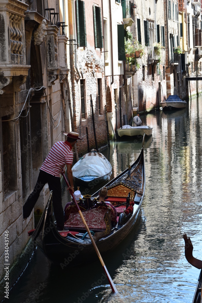 Gondola driver with passengers pushing the gondola away from a building’s wall with his feet on an empty canal