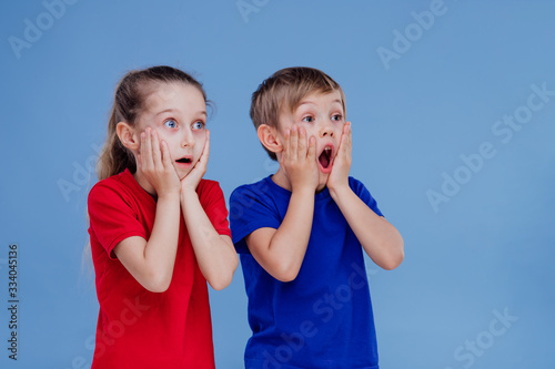 Obraz na plátne Astonished little girl and boy in casual clothes holding hands on faces and look