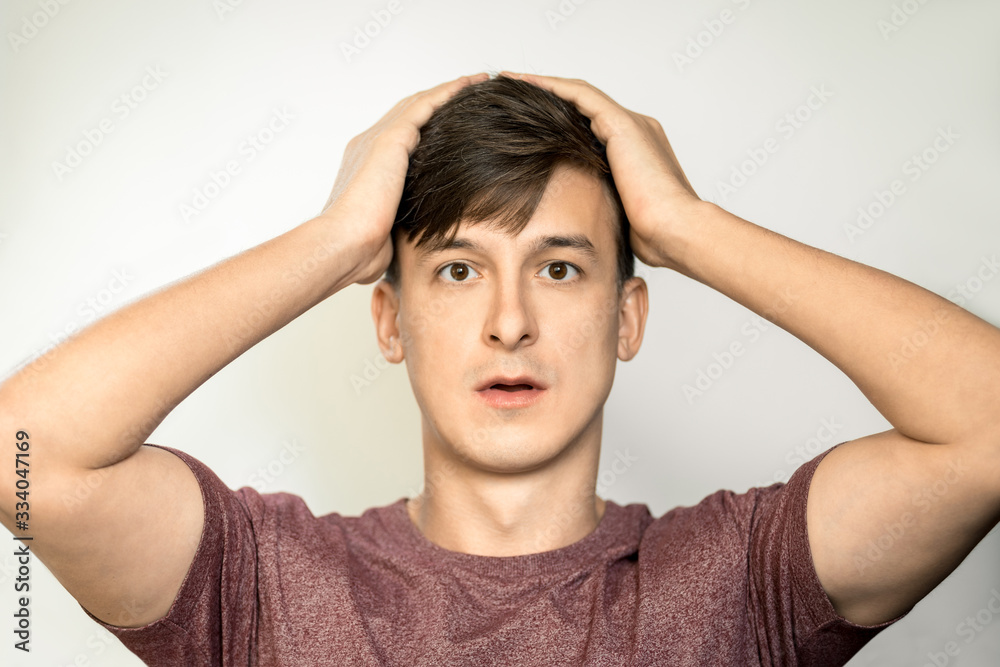 Portrait of a young man with dark hair with a surprised face holds his head. Horizontal frame Portrait of a young man with dark hair with a surprised face holds his head. Horizontal frame
