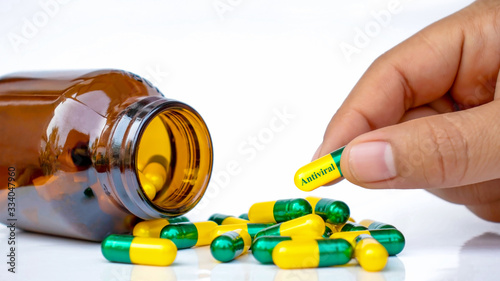 Quadro su tela The girl's hand picks up an antiviral capsule (the coronal virus, or covid-19) that runs out of the bottle on a white background