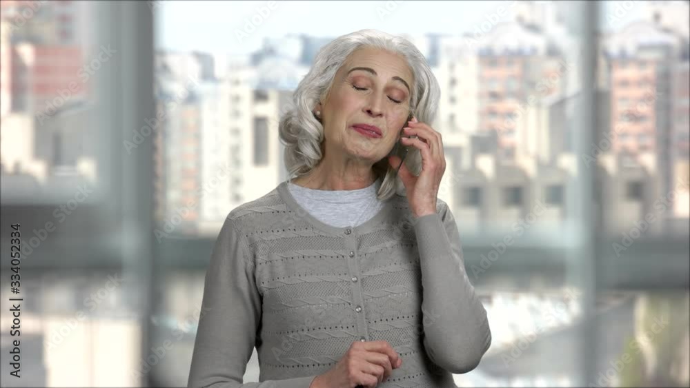 Old lady calling and talking on transparent phone with copy space. Senior woman accepting phone call indoor in office, windows background. Old lady calling and talking on transparent phone with copy space. Senior woman accepting phone call indoor in office, windows background.