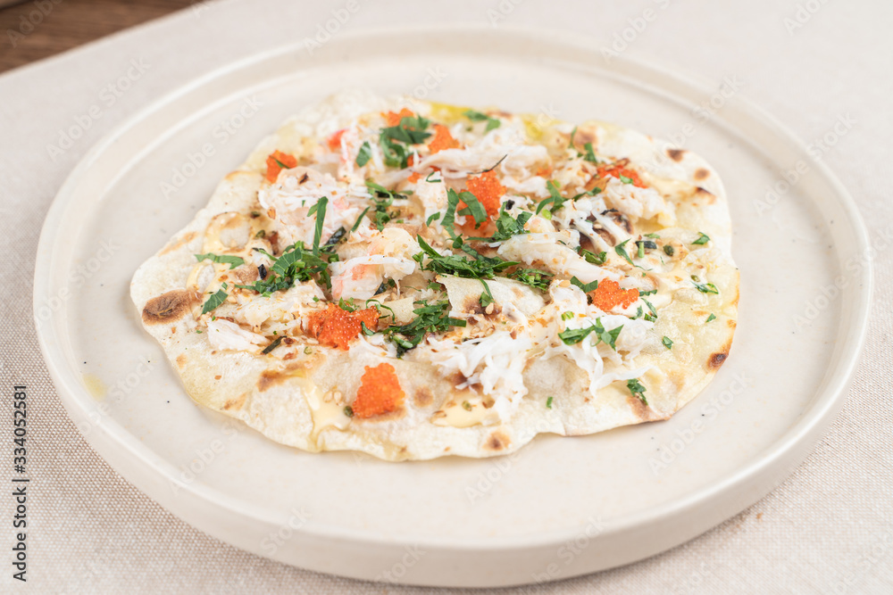 Wheat crunchy tortilla with crab meat, greens and red caviar in a seafood restaurant