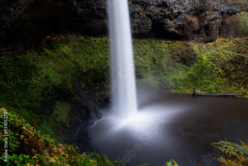 Long exposure of a waterfall at Silver Falls State Park  Silverton  Oregon  USA  in the Autumn  featuring yellow and green colors and a cave
