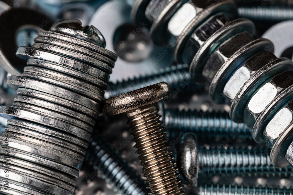 A Macro shot of the Threads of a small stainless steel bolt on a pile of washers, nuts and bolts.  Strong Contrast