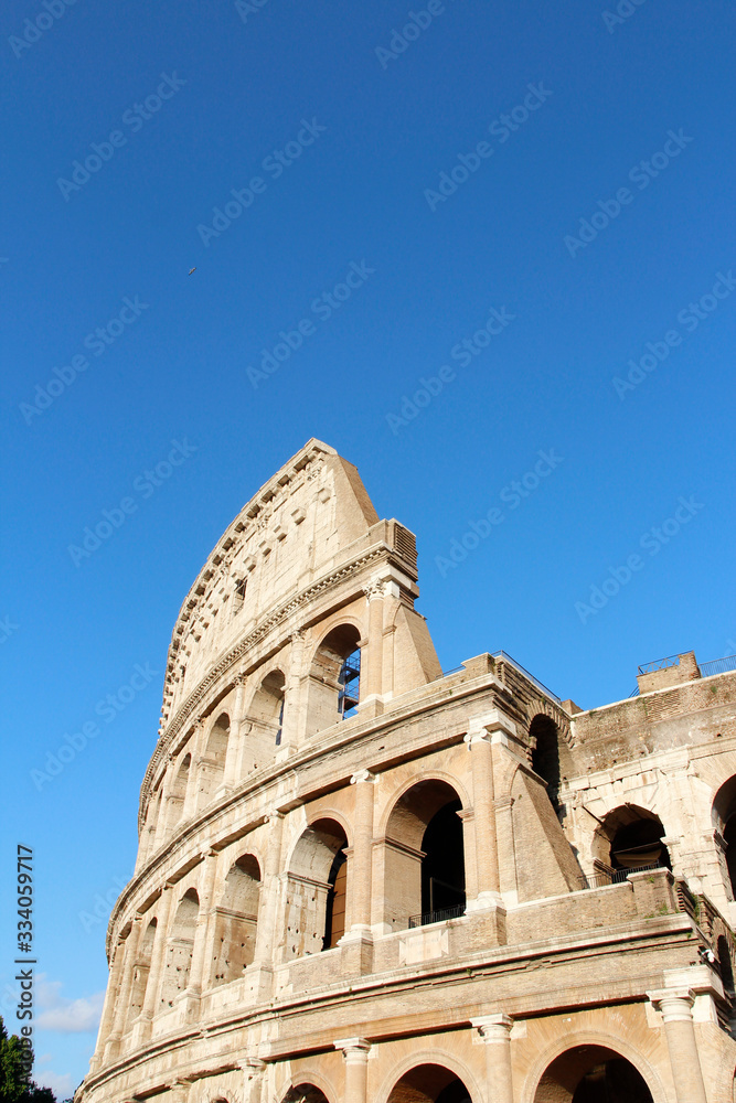 The exterior facade of the Colosseum or Coliseum with the arches against blue clear sky in Rome, Italy