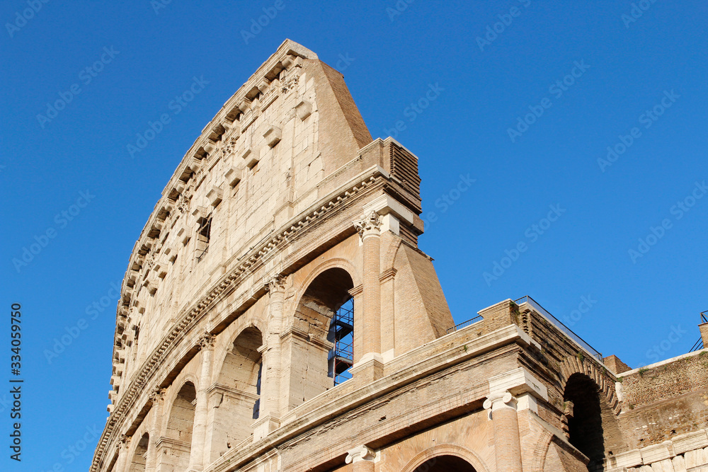 The exterior facade of the Colosseum or Coliseum with the arches against blue clear sky in Rome, Italy