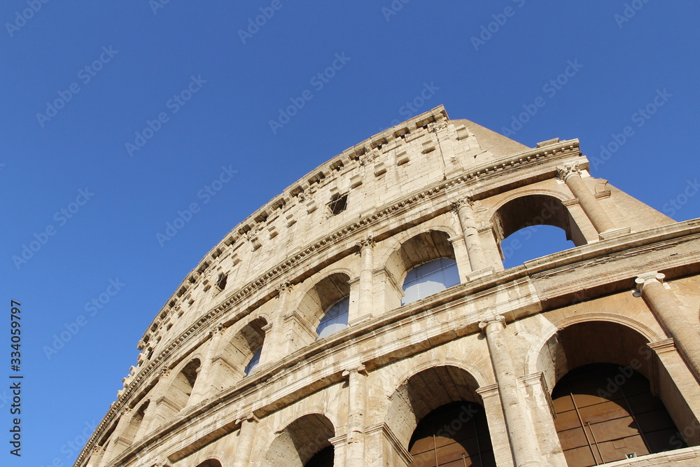 The exterior facade of the Colosseum or Coliseum with the arches against blue clear sky in Rome, Italy