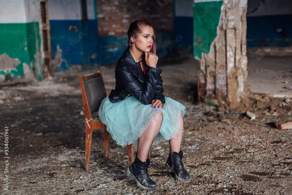 Portrait of a young girl with pink hair sitting old the old chair inside of collapsed building surrounded by ruins