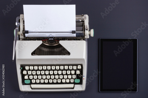 Old retro typewriter with blank paper and modern tablet on a black table. Technologies of different eras. The evolution of technology. Concept of blogging, remote work or freelancer.