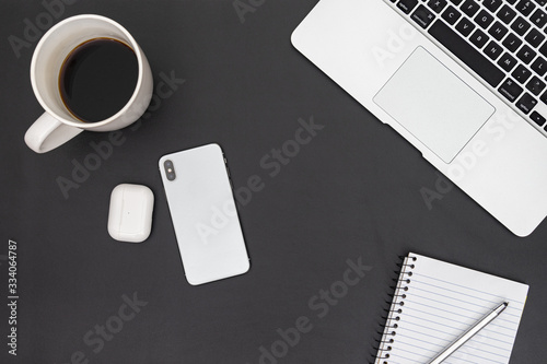 Modern workspace with coffee cup, notebook, pen, laptop, smartphone and bluetooth earbuds on black leather desk pad. Top view. Flat lay style.