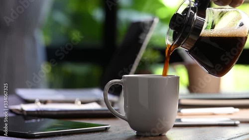 A hand pouring steaming coffee in to a cup on a work desk when work from home