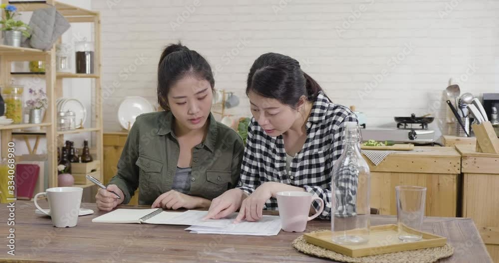 two young girl friends managing finances at home. korean ladies reviewing their bank accounts using calculator while sit at modern kitchen. women roommates doing paperwork together in apartment. two young girl friends managing finances at home. korean ladies reviewing their bank accounts using calculator while sit at modern kitchen. women roommates doing paperwork together in apartment.