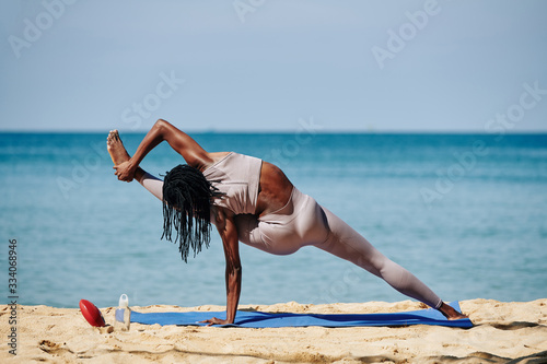 Fit stong young woman doing Visvamitrasana, she is extending leg out to the side and catch hold of foot with hand photo