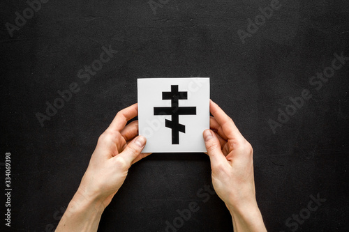 Christianity. Ortodoxal cross in hands on black background top-down copy space