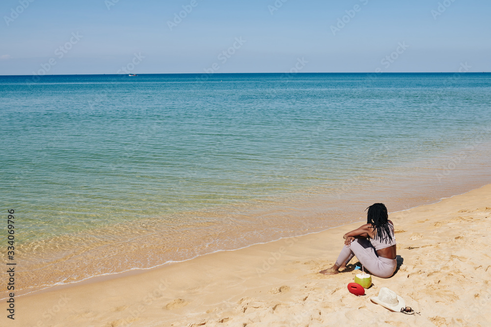 Young woman in sports top and legging sitting on beach and enjoying the view of beautiful seascape Young woman in sports top and legging sitting on beach and enjoying the view of beautiful seascape