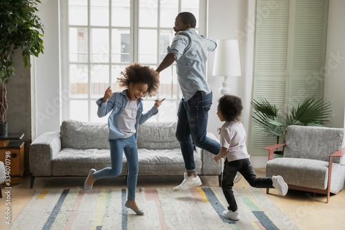 Active african funny dad little son and crazy daughter heavy metal or rock and roll lovers dancing in cozy living room relish life fooling around listening cool music scream with joy enjoy party hard photo