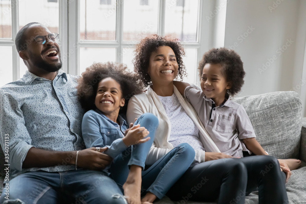African couple with little kids enjoy communication telling jokes laughing resting on sofa. Concept of healthy happy family, first dwelling or new home, leisure weekend activities with children indoor African couple with little kids enjoy communication telling jokes laughing resting on sofa. Concept of healthy happy family, first dwelling or new home, leisure weekend activities with children indoor