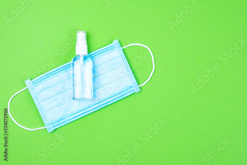 Top view of disposable medical surgical protective face mask with antibacterial antiseptic spray for hands sanitizer on green background. Protection against virus, flu or coronavirus . Copy space.