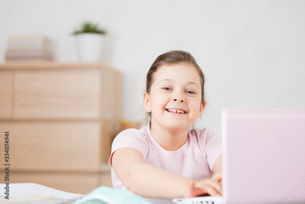 A smiling girl at a pink computer,laptop sits at an online training session, a happy schoolgirl is delighted with distance online training.Online concept of school education and social distance during A smiling girl at a pink computer,laptop sits at an online training session, a happy schoolgirl is delighted with distance online training.Online concept of school education and social distance during