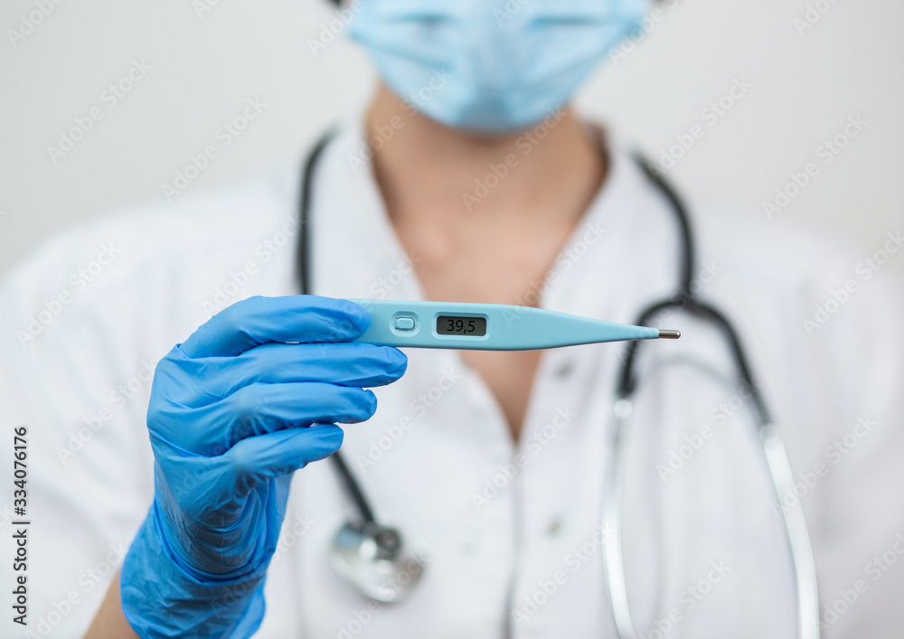 Close-up of a hand in a rubber latex medical blue glove holding an electronic thermometer in a mask. The concept of fever, malaise, fever, pain, coronavirus. Isolated on a white background. Close-up of a hand in a rubber latex medical blue glove holding an electronic thermometer in a mask. The concept of fever, malaise, fever, pain, coronavirus. Isolated on a white background.