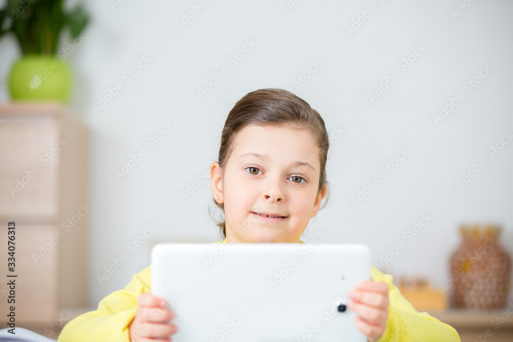 Distance learning online education.Smiling schoolgirl girl with a white tablet at home studying lessons.Online concept of school education and social distance during quarantine, self-isolation Distance learning online education.Smiling schoolgirl girl with a white tablet at home studying lessons.Online concept of school education and social distance during quarantine, self-isolation