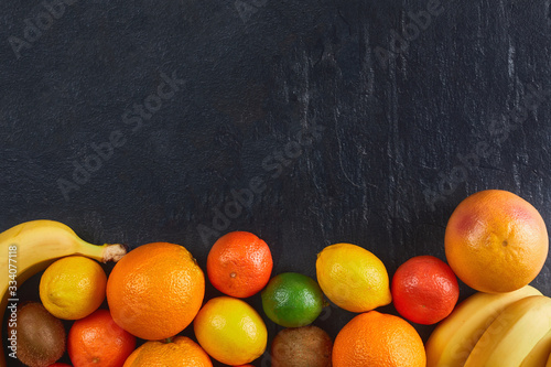 Assortment of tropical fruits orange, tangerine, banana, grapefruit, lime, kiwi on dark background. Fresh fruit set. © wertinio