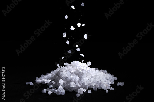 Sea salt crystals fall on a pile of salt, black background