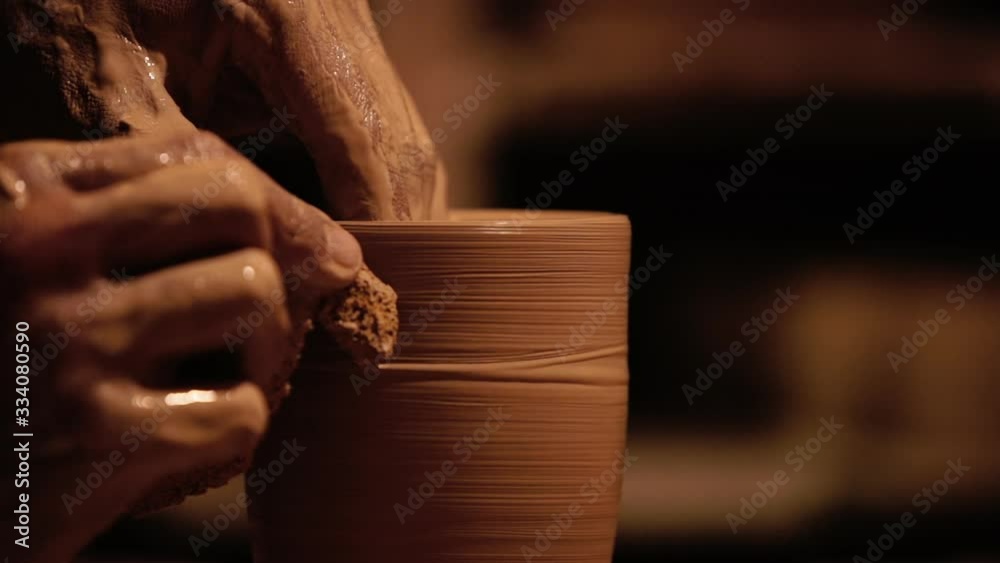 Young handsome sculptor shapes the clay product with pottery tools. Artisan potter prepares material for his pottery. Strong man hands working clay on potter's wheel. Work close-up.
