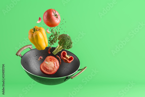 Fresh colored vegetables flying from the wok. Green studio background