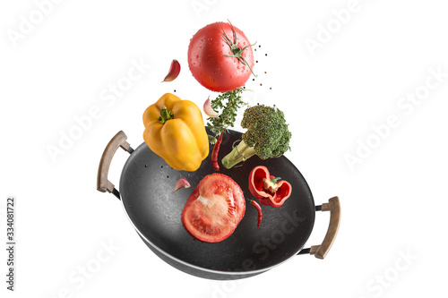 Fresh multicolored vegetables fly over a wok frying pan. White isolated background.