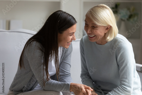 Overjoyed senior mother and grown-up adult daughter sit on couch in living room have fun talking, happy mature mom and millennial girl child relax on sofa at home together, chat and gossip laughing © fizkes