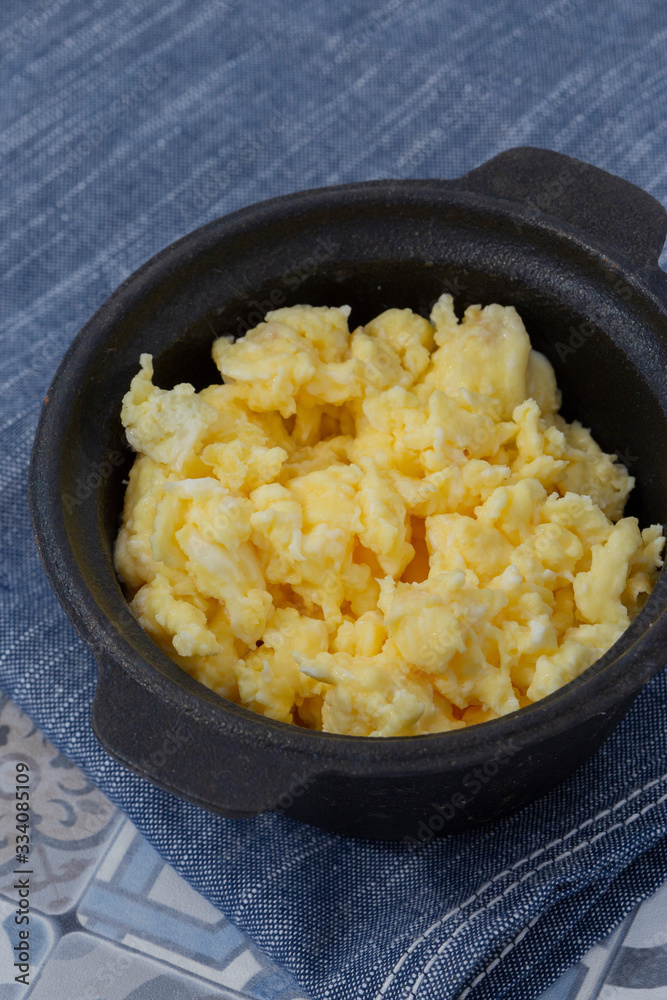 Scrambled egg in a traditional cast iron pot on a blue tea towel. On a patterned tile surface Scrambled egg in a traditional cast iron pot on a blue tea towel. On a patterned tile surface