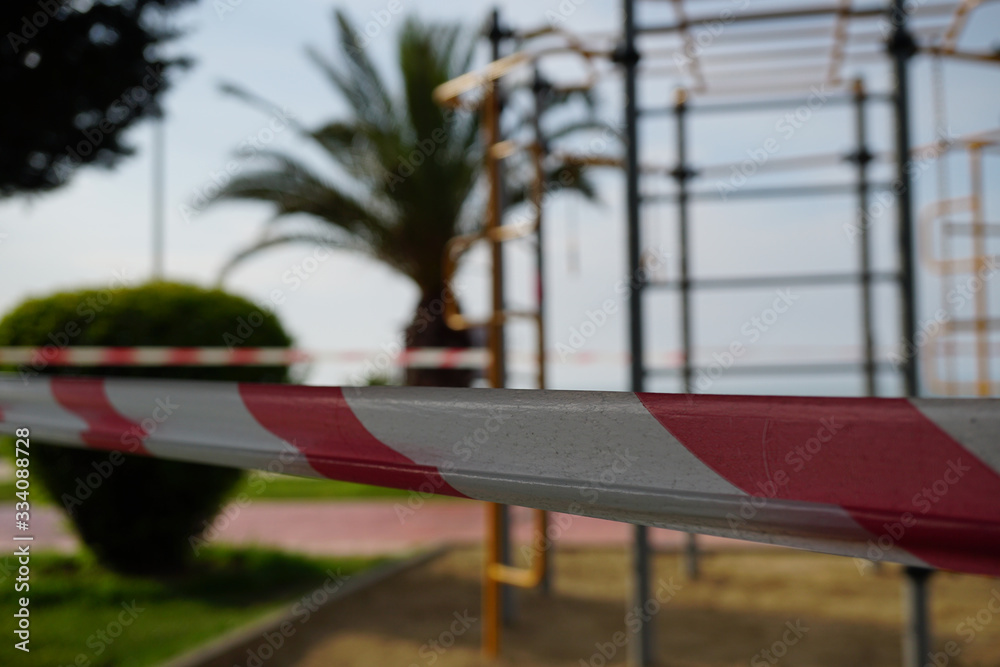 Fototapeta premium Barrier red and white tape closing a passage to a street sports ground, shot close-up on a background of sports equipment. COVID-19 pandemic.