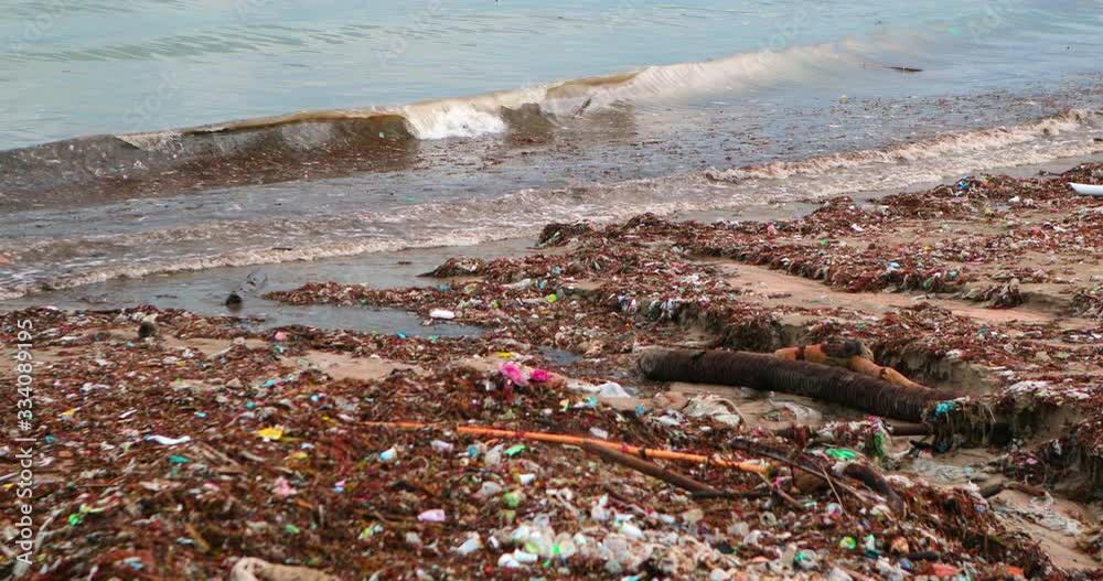 Plastic Trash And Garbage Dumped On Dark Sand Of The Beach And Floating
