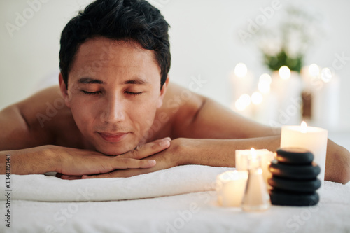 Smiling mature man resting after spa masage and enjoying atmophere of spa salon and tasty smell of burning candles photo