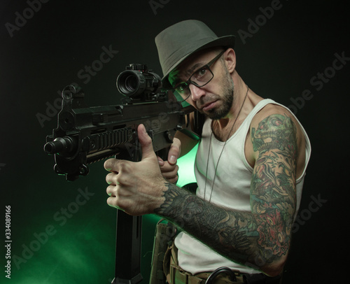 a sporty guy with a tattoo poses with an automatic rifle