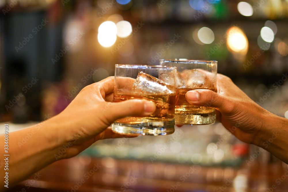 Two men clinking glasses of whiskey drink alcohol beverage together at counter in the pub                    